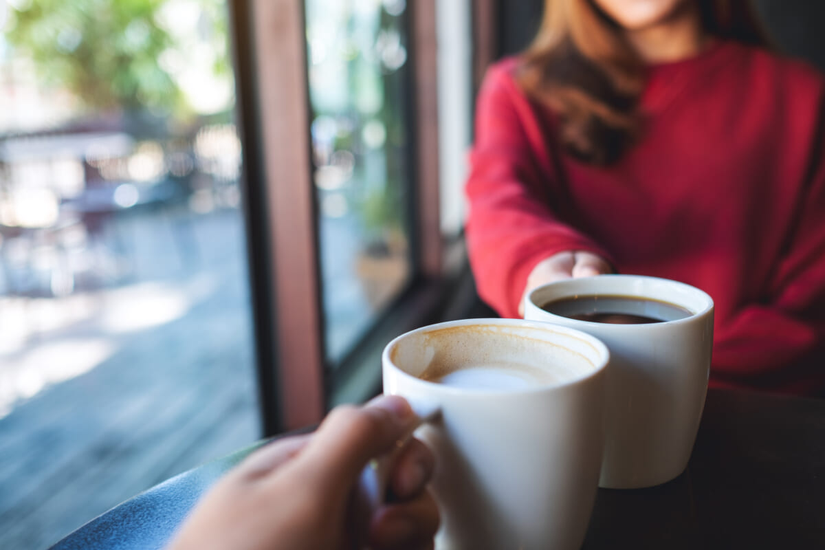 Closeup image of a man and a woman clinking coffee cups together | コーヒーステーション