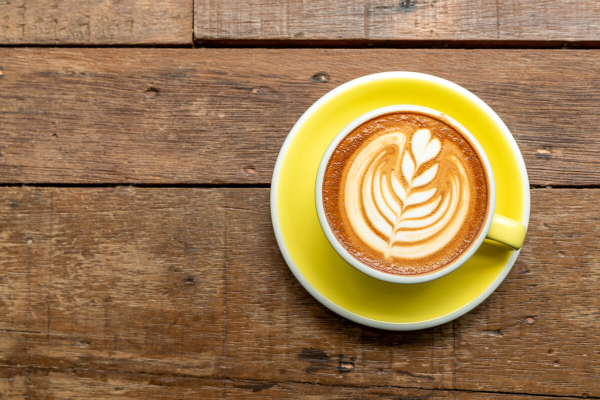 Top view of hot cappuccino coffee in a yellow cup with latte art on wooden table background | コーヒーステーション