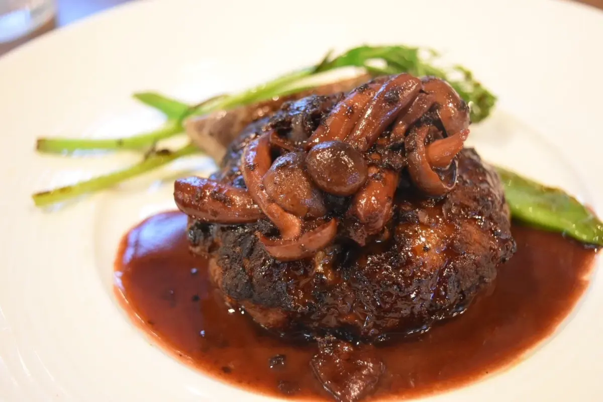 白い皿に盛られた、きのこがたっぷり乗ったハンバーグステーキ