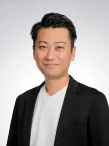 Head and shoulders portrait of a smiling man wearing a black blazer and white shirt against a light gray background