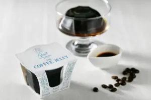 Packaged coffee jelly with a glass of coffee and scattered coffee beans on a white surface
