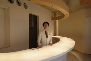 Man in a white suit standing behind a curved white reception desk in a modern interior space