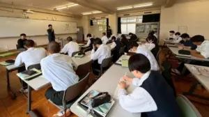 2871926a91b2fc017a7821536c8a0d5f | コーヒーステーション Students in uniforms sit at desks in a bright classroom listening to a teacher at the front by a whiteboard