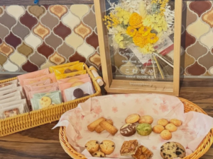 29bb9e674ebbd4da318cc6c17accafe0resized857x643 | コーヒーステーション Basket of assorted cookies and pastries on a wooden table with a framed yellow flower bouquet in the background