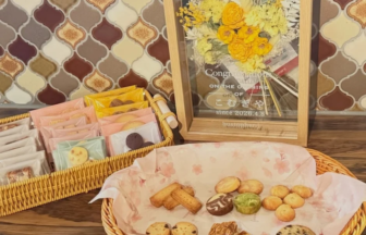 Basket of assorted cookies and pastries on a wooden table, with a framed yellow flower bouquet in the background.