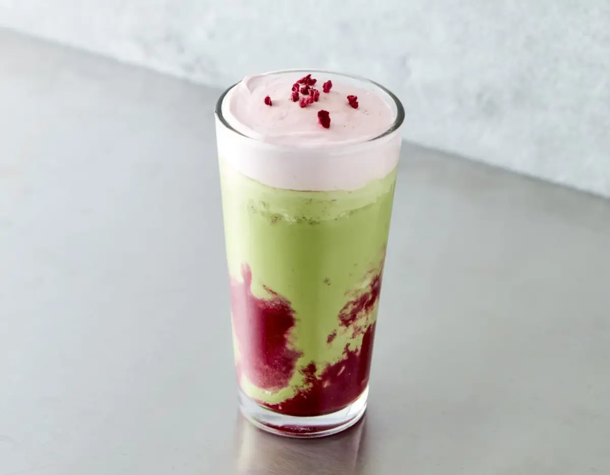 緑色の抹茶と赤色のベリーソースが層になったドリンクで、上にはピンク色のホイップクリームと小さな赤い粒がトッピングされている