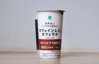 Canned caffe latte drink with Japanese text on a white and maroon label, standing on a wooden table.