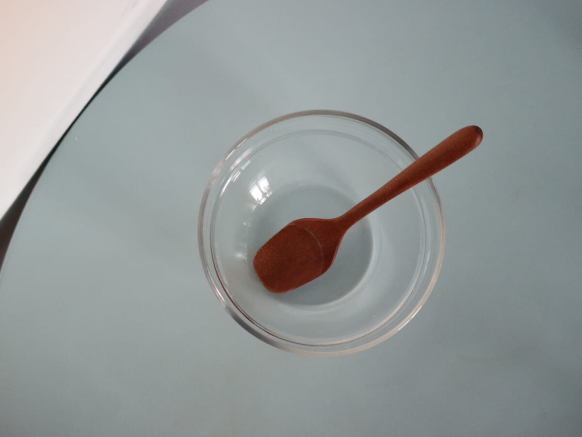 Clear glass bowl with a brown wooden spoon resting inside on a light blue surface top down view