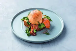 4203bf40045e0774eddc07f366ce2617 | コーヒーステーション Poached egg atop toasted bread with sautéed greens crispy bacon and a slice of smoked salmon on a pale blue plate
