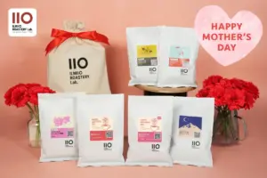 Gift setup of Ilmio Roastery Lab coffee bags and a beige gift bag with a red bow for Mothers Day against a pink background 