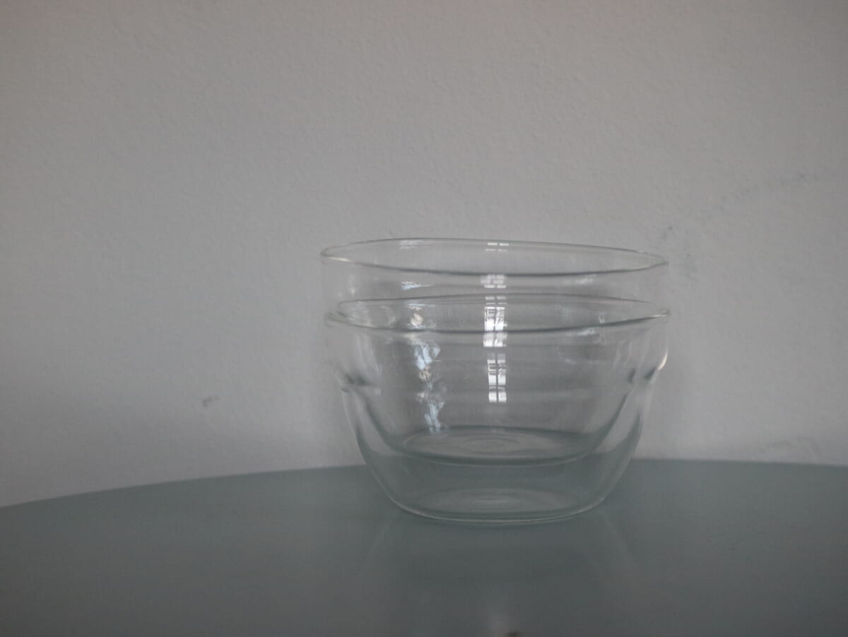 Two clear glass bowls stacked on a pale table against a white wall empty and clean
