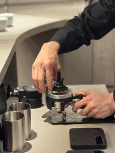 Barista tamping freshly ground coffee into a portafilter on an espresso machine at a cafe