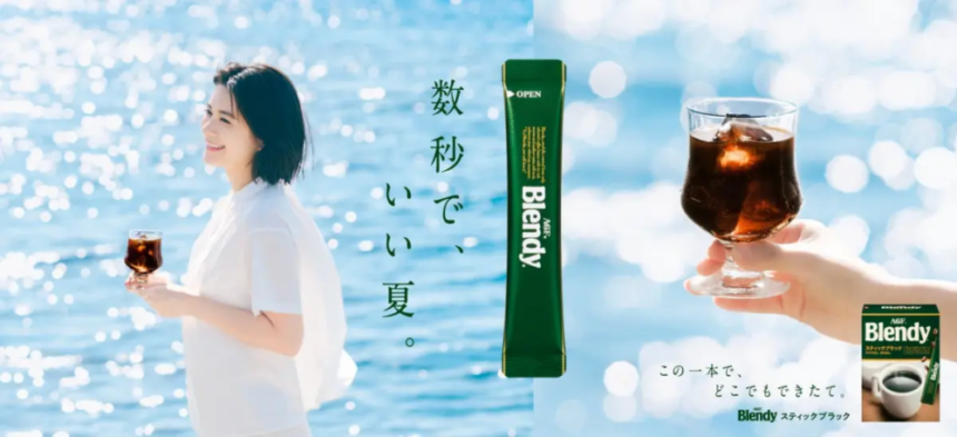 Woman standing by a sunny sea holding a small glass of coffee with a vertical green Blendy sachet in the center and a hand holding a glass on the right Japanese slogan text nearby