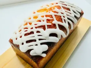 4eb94ea563a42411fd8c7a20b6c594a6 | コーヒーステーション Loaf cake with a white lattice drizzle on top resting on a wooden board