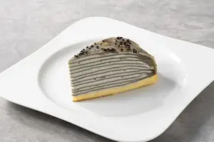 Slice of gray layered crepe cake on a white plate topped with black sesame seeds