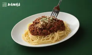 5372d21db8429e0d8b1737a646e6b23e | コーヒーステーション Plate of spaghetti with meat sauce topped with grated cheese on a white oval dish green table background fork resting on pasta