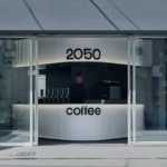 Futuristic coffee shop counter visible through glass doors with 2050 above and coffee on the front panel