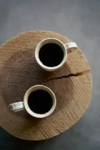 54512c1bed259953ca0d33ba28e159c3 | コーヒーステーション Top down view of two white ceramic mugs filled with black coffee on a wooden tree stump table