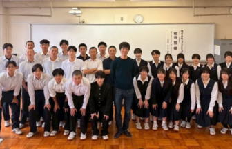 Group of students in uniforms posing with a man in the center in a classroom setting, smiling for a class photo.