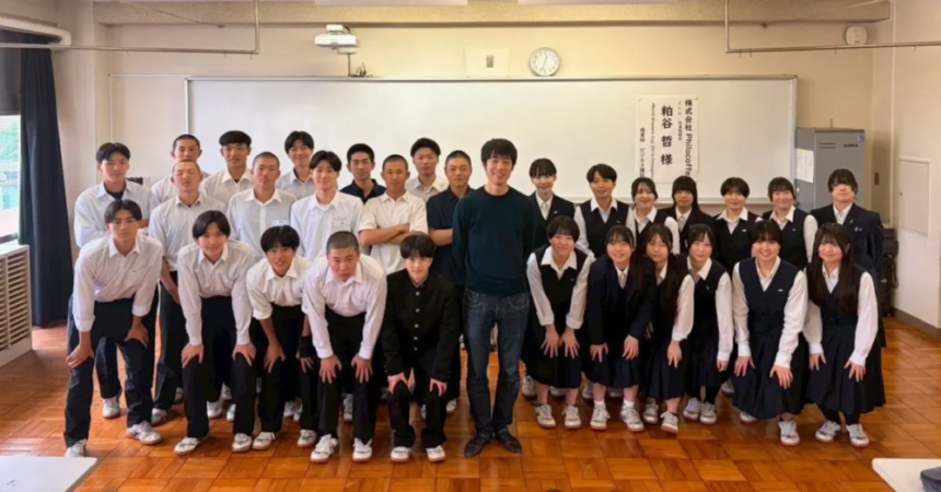 Group of students in uniforms posing with a man in the center in a classroom setting smiling for a class photo