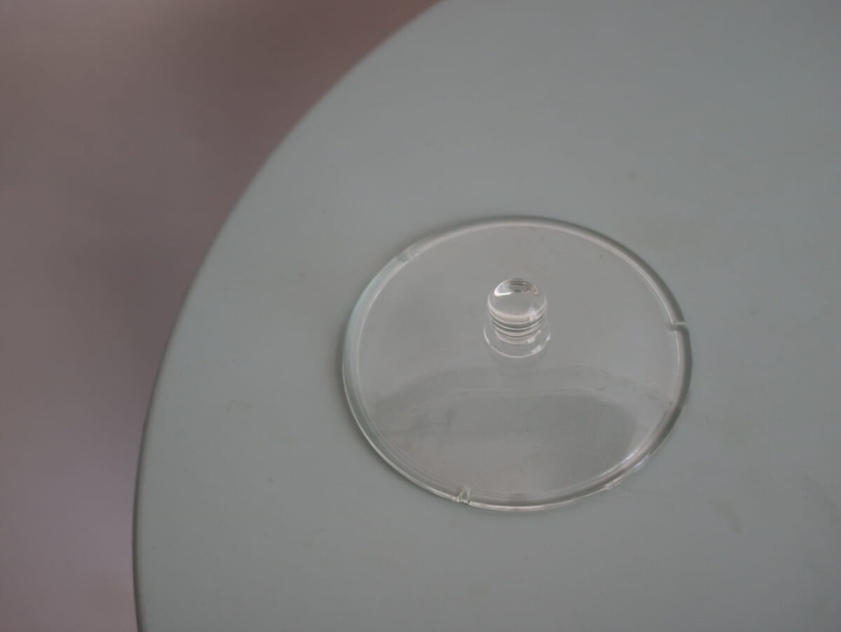 Close up of a clear plastic lid with a small central knob on a pale gray surface