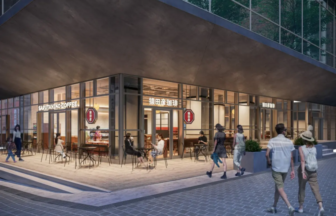 Modern cafe storefront with glass walls, outdoor seating, and pedestrians along a paved sidewalk under a large overhang.