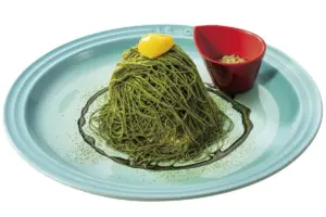 Mound of green pesto spaghetti on a turquoise plate topped with a small yellow butter square and a red dipping cup