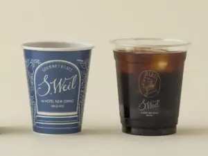 Two disposable cups side by side a blue SWeil cup on the left and a clear plastic cup of iced coffee on the right both labeled with the SWeil logo