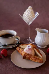 Croissant split with a scoop of strawberry ice cream on a plate HaagenDazs label visible beside a cup of coffee and a white creamer