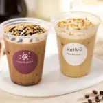 Two iced coffee drinks with whipped cream on a white plate left with chocolate drizzle right with nuts and a cream topping