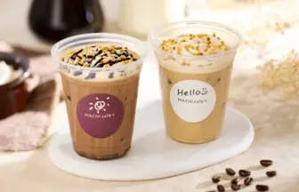 Two iced coffee drinks with whipped cream on a white plate; left with chocolate drizzle, right with nuts and a cream topping.