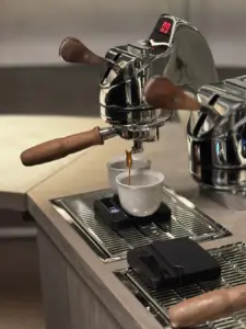 Espresso machine pouring dark coffee into a white cup on a metal countertop professional setup with wooden handled levers nearby