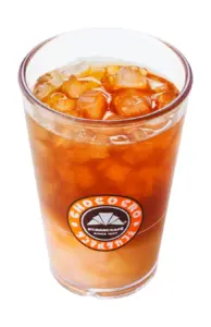 Tall glass of iced coffee with ice cubes orange brown liquid featuring a St Marc Café logo on the side