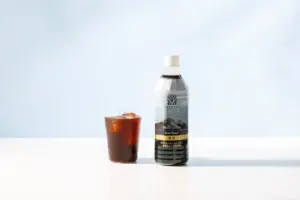 82281b9643ba6c8502506f665f6a0721 | コーヒーステーション Bottle of Maruyama Black Coffee Dark Roast next to a glass of iced coffee on a white surface