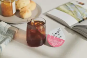 Glass of iced coffee with ice cubes beside a pink Seasonal Blend coffee capsule tag on a white counter