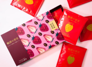 826c8df3f3fc9425872d2dd5db1b1d30resized883x643 | コーヒーステーション Flat lay of a pink box with strawberry pattern surrounded by red packets with yellow strawberry illustrations suggesting strawberry flavored coffee gifts