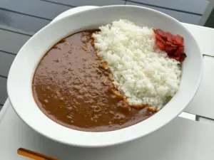 Plate with white rice and brown curry with pickled red garnish on the side