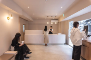94a9eb7fb9dda0f8cb68e025bc15c719resized963x643 | コーヒーステーション Minimalist cafe reception with a white counter staff talking to a customer and a seated person on the left sipping from a cup
