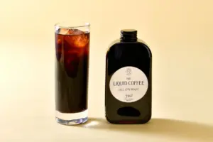 Bottle of The Liquid Coffee Full City Roast beside a tall glass of iced coffee on a pale background