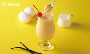 955e1f7a5acd74d31ed2dcfd8ef7a6d7 | コーヒーステーション Creamy yellow beverage in a tall glass topped with a cherry with vanilla beans and a milk pitcher nearby on a bright yellow background
