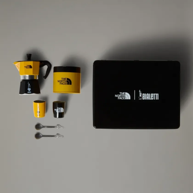 Collaboration coffee set yellow and black Moka pot two small cups spoons and a black box with The North Face and Bialetti logos on a gray background