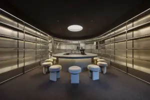Circular bar in a sleek metal walled lounge surrounded by white padded stools