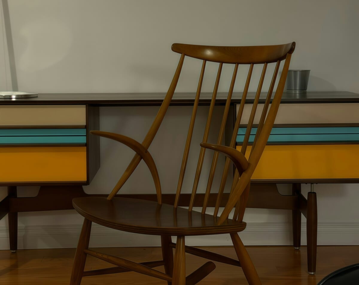Wooden Windsor chair with a tall spindle back in front of a retro desk with orange and teal drawers