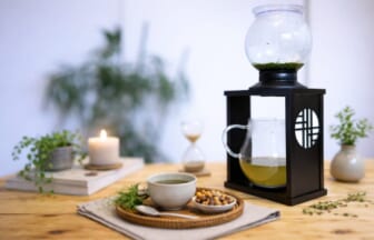 Cozy tea setup on a wooden table glass kettle inside a black lantern a mug of tea bowl of nuts candle hourglass and plants