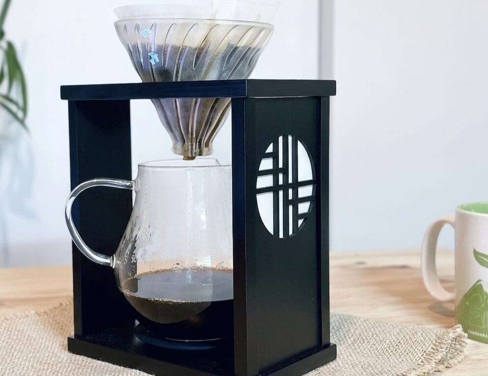 Black coffee dripper stand with glass carafe and metal pour over cone ready for brewing on a wooden table