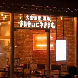 Night view of a brick walled restaurant interior through glass doors with glowing JapaneseChinese sign above the entrance and warm lights inside