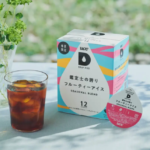 Seasonal blend Drip Pod box beside a glass of iced coffee on a light table with a vase of greenery in the background