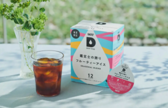 Seasonal blend Drip Pod box beside a glass of iced coffee on a light table, with a vase of greenery in the background.