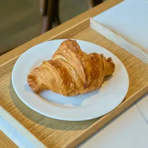 Golden croissant on a white plate set on a light wooden tray