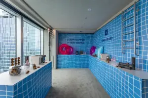 Retail space with blue tiled walls displaying sunglasses on white counters large windows city view and pink rings as decor informative image